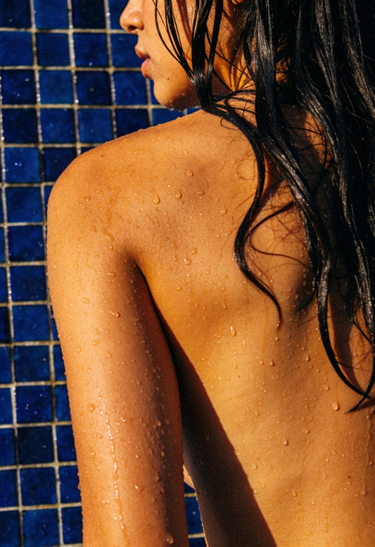 Mujer de espaldas con el cabello mojado, frente a una pared de mosaico azul cobalto